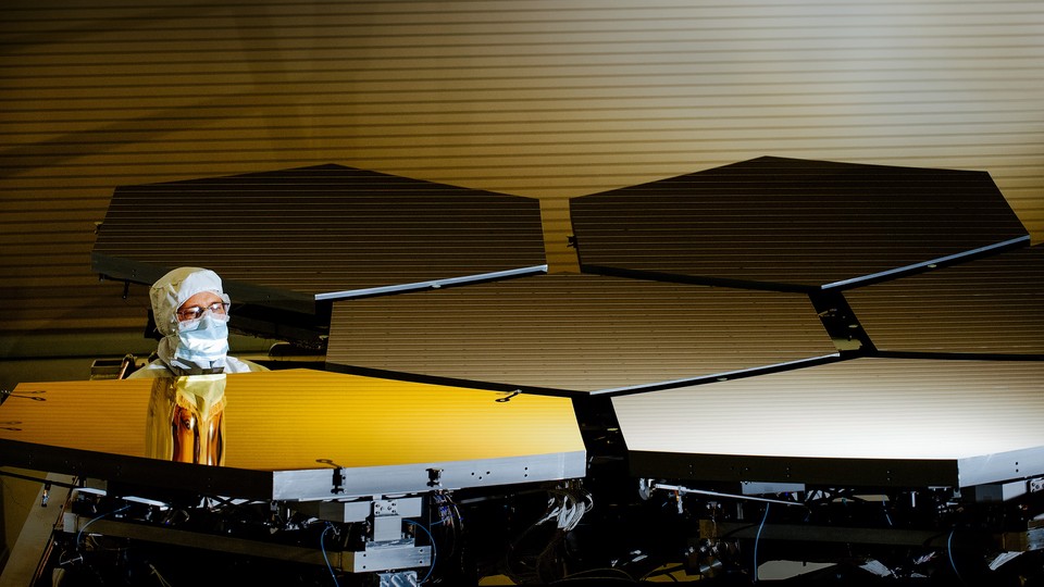 A technician, dressed in protective clothing, examines several of the James Webb Space Telescope's mirrors.