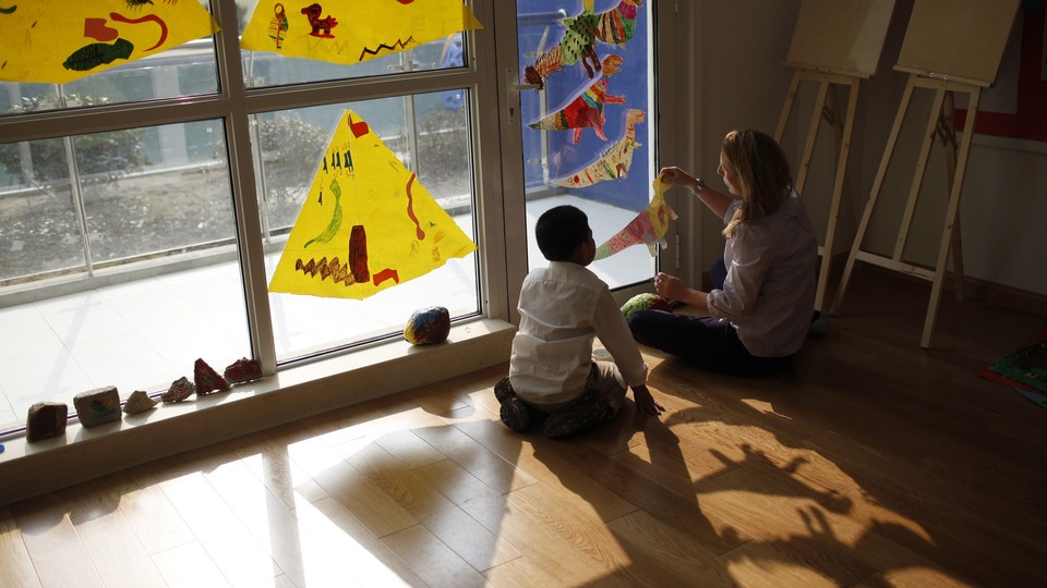 A child and adult sit together on the floor, playing with construction-paper dinosaurs.