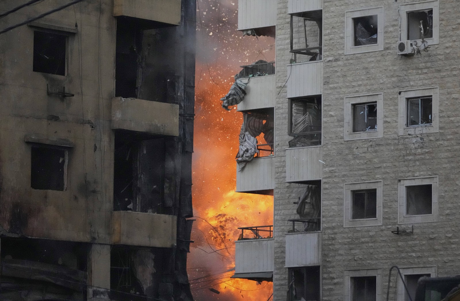 Flames and smoke from an airstrike are visible between tall buildings.
