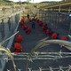 Detainees in orange jumpsuits sit in a holding area under the watchful eyes of military police during in-processing to the temporary detention facility at Camp X-Ray of Naval Base Guantanamo Bay on January 11, 2002.