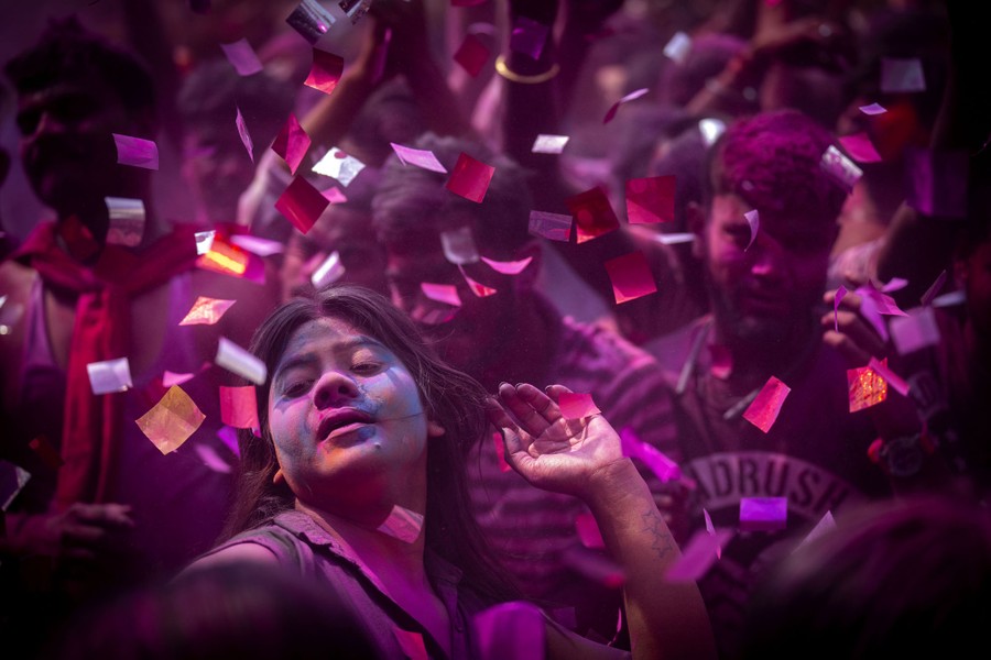 People celebrate in a crowd, among confetti and colored dust.