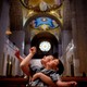 A woman holds a child in her arms as they both look up toward the ornate ceiling of a basilica.