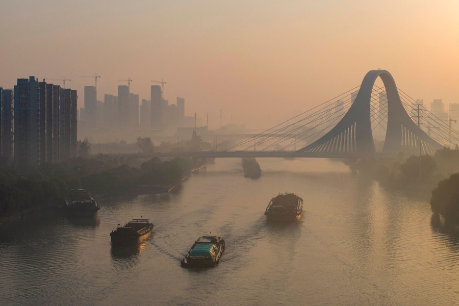 Barges sail on a misty canal through a city in China.