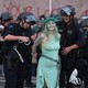 Police officers in riot gear arrest a protester dressed as Lady Liberty in chains.