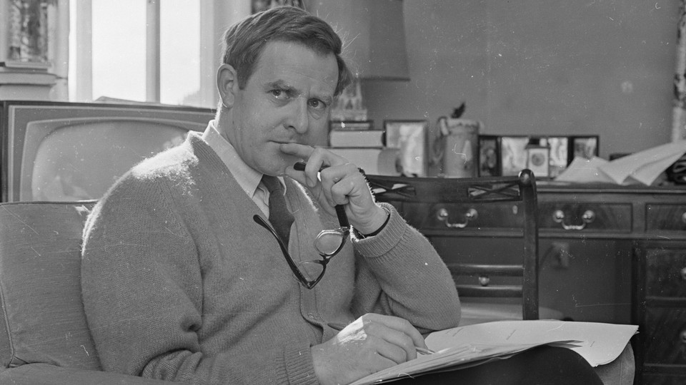 John le Carré is pictured sitting at an armchair with a notepad on his lap in March 1965.