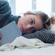A woman stares at her phone in bed.