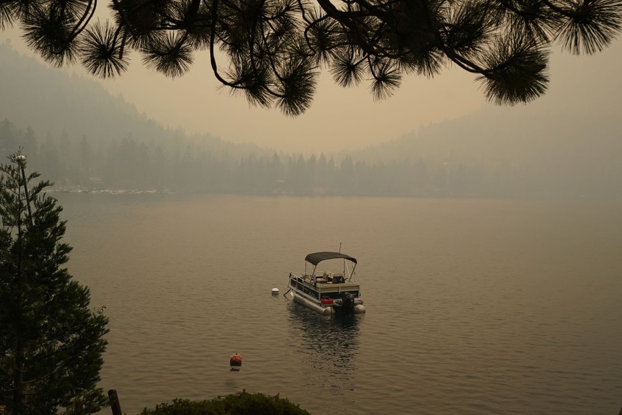A pontoon boat floats in a lake with the hills in the background obscured by smoky sky.