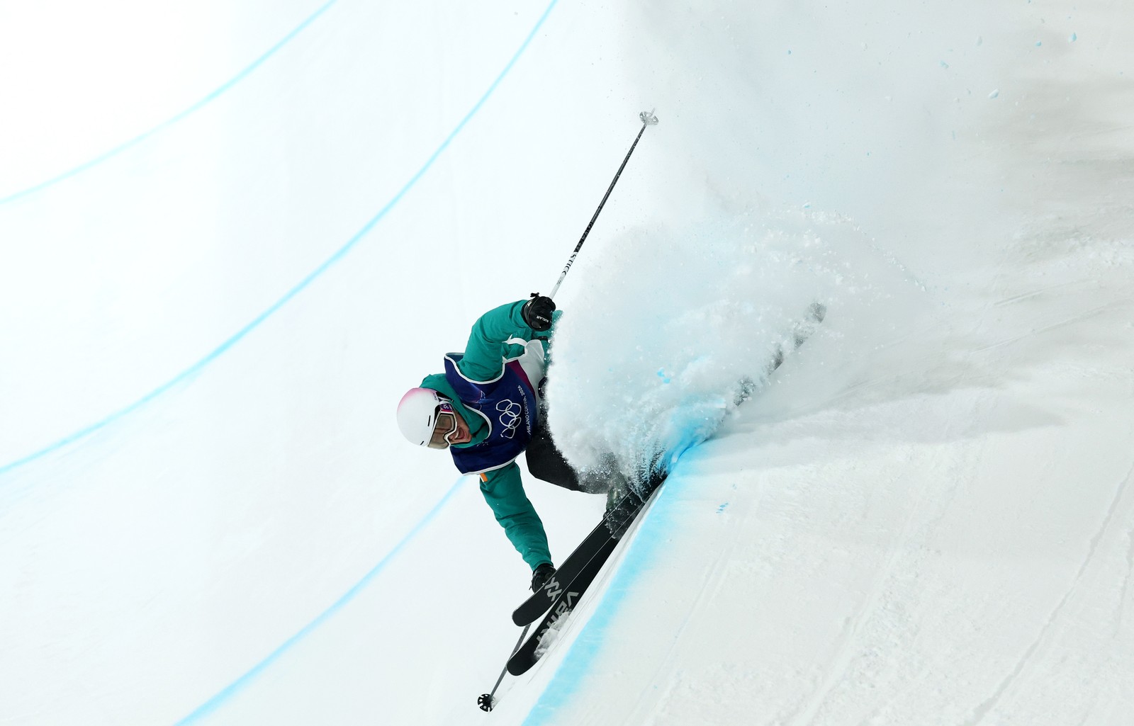 A freestyle skier grinds along the lip of an Olympic halfpipe, kicking up snow.