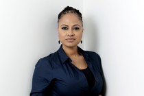 Ava DuVernay stands against a white background in a dark blue shirt