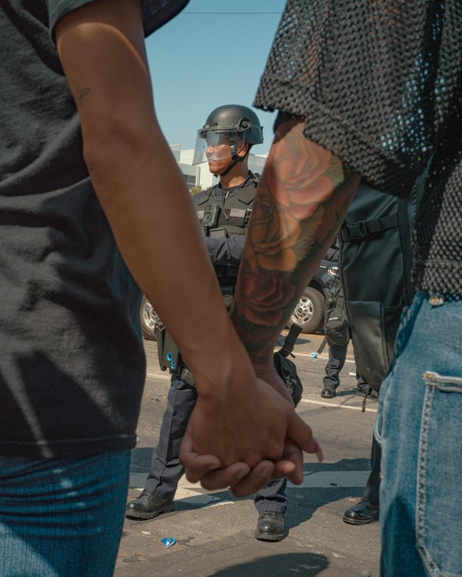 Two people hold hands in front of a police officer