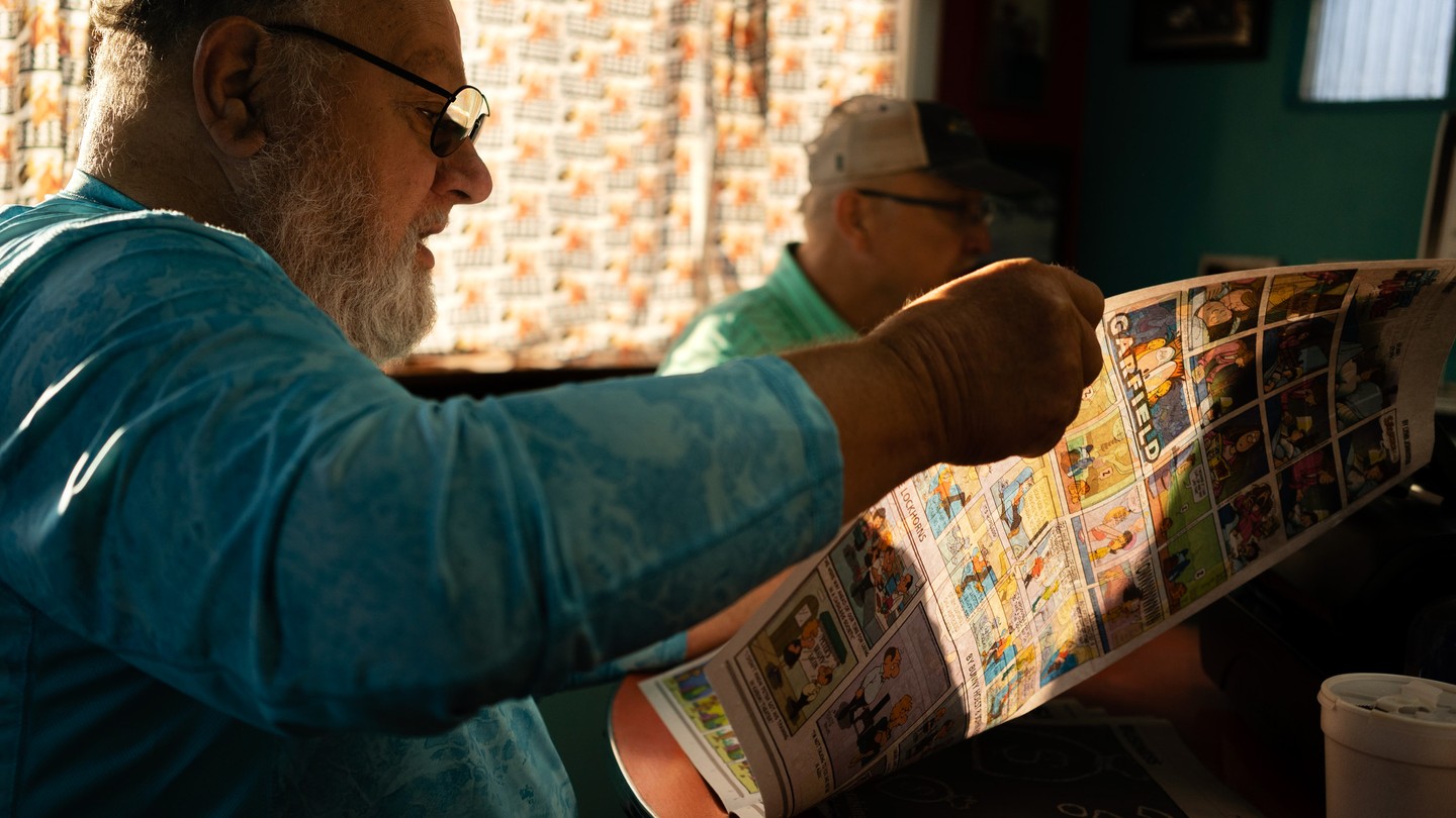 A man is reading The Hawk Eye newspaper in a diner.