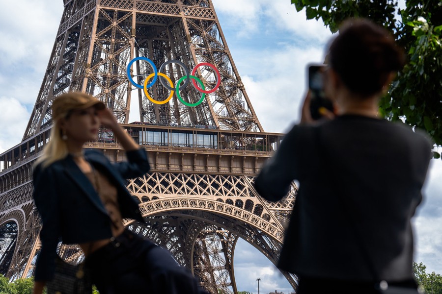 Tourists take pictures near the Eiffel Tower, which is decorated with the Olympic rings.
