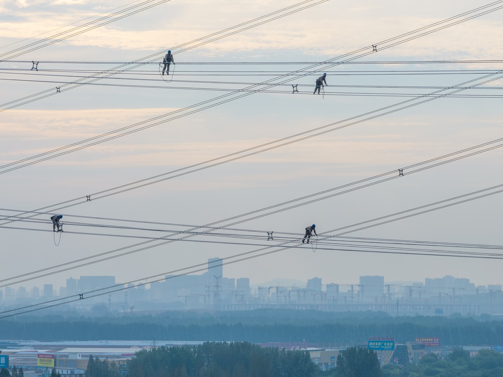 Four workers walk along power lines high up in the sky.