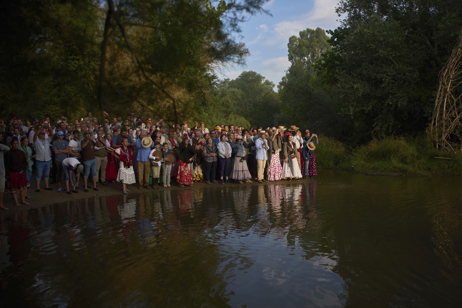 A crowd of people gather on a river shoreline.