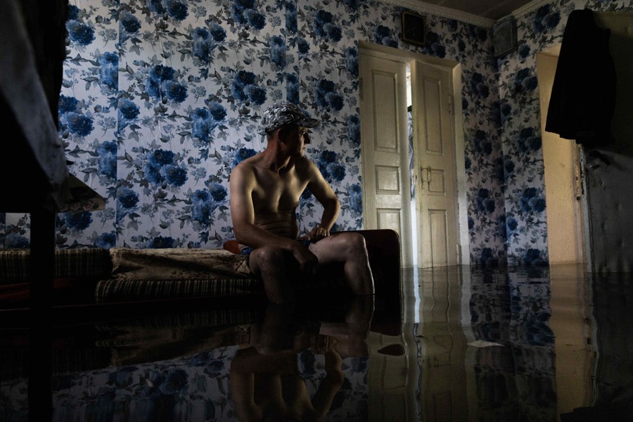 A person sits on a bed inside a flooded room.