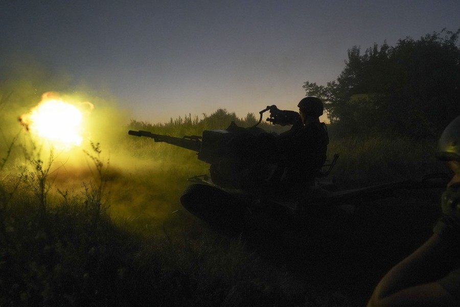 A soldier fires an anti-aircraft gun low to the ground in a field.