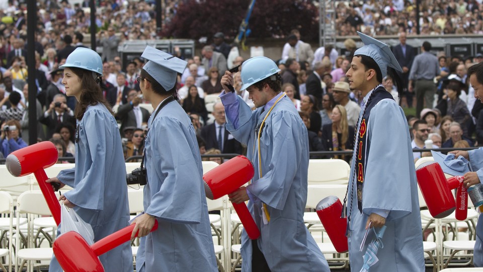 Four students walk in light blue commencement caps and gowns.