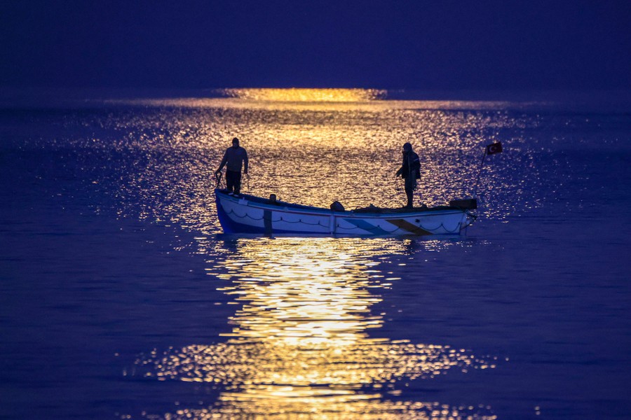 Two people stand in a small boat on a moonlit lake.