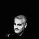 A black-and-white photo of Qassem Soleimani, looking downward to the left of the camera