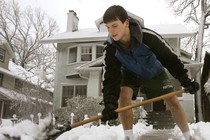 A boy shoveling snow while wearing shorts.