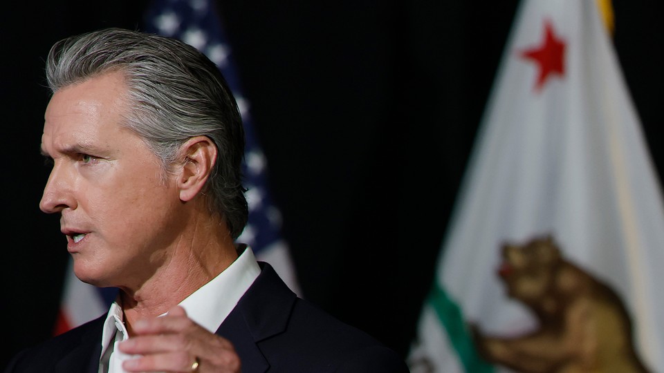 Color photograph of Gavin Newsom speaking with U.S. and California flags behind him.