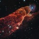 A long, billowing, and glowing cloud of material, seen in deep space, backdropped by stars and more-distant galaxies.