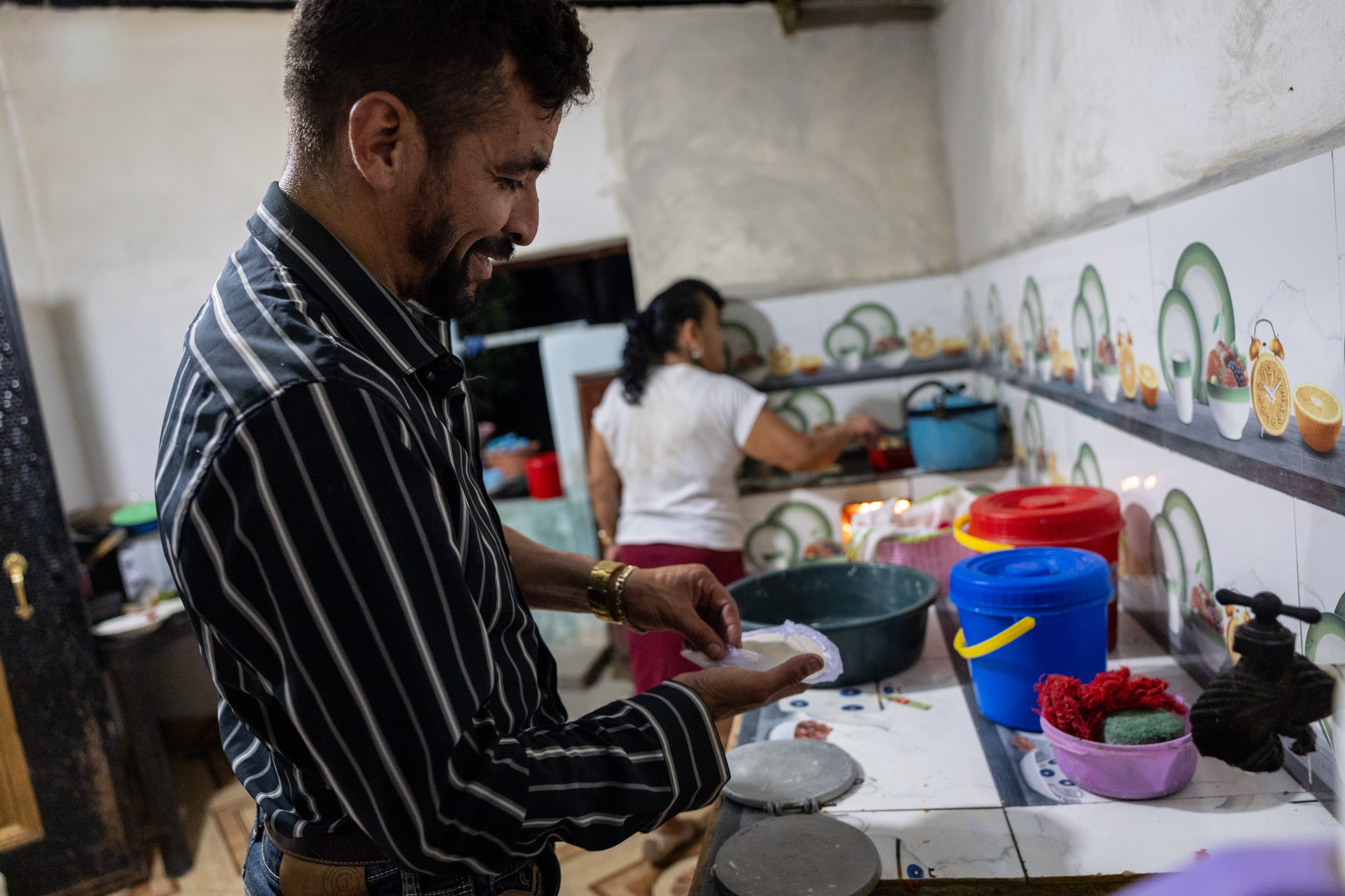 A man makes tortillas in a kitchen with his mother.