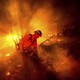 A firefighter works on a forest fire among smoke and embers at night.