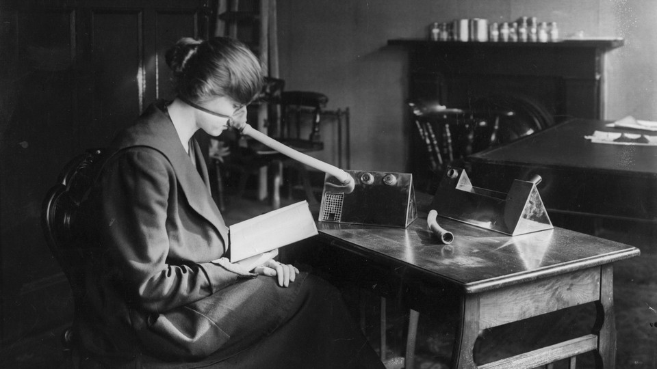 A woman sits reading a book while wearing a flu mask.