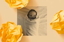 A black-and-white photo of a sleeping infant wrapped in a light colored blanket is surrounded by three pieces of yellow crumpled-up paper