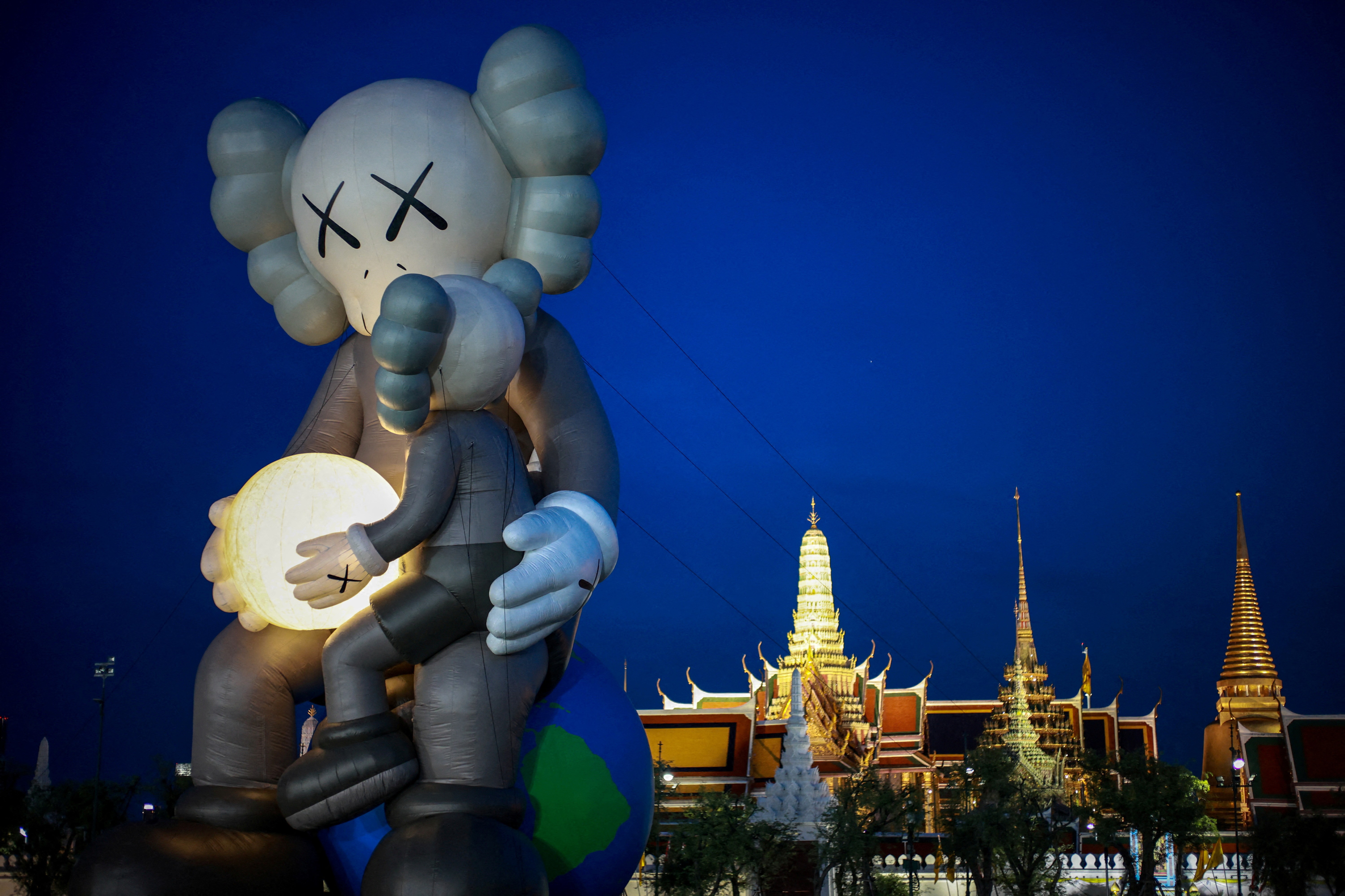 A large inflated art installation, shaped like two anthropomorphic figures holding a small moon in their hands.