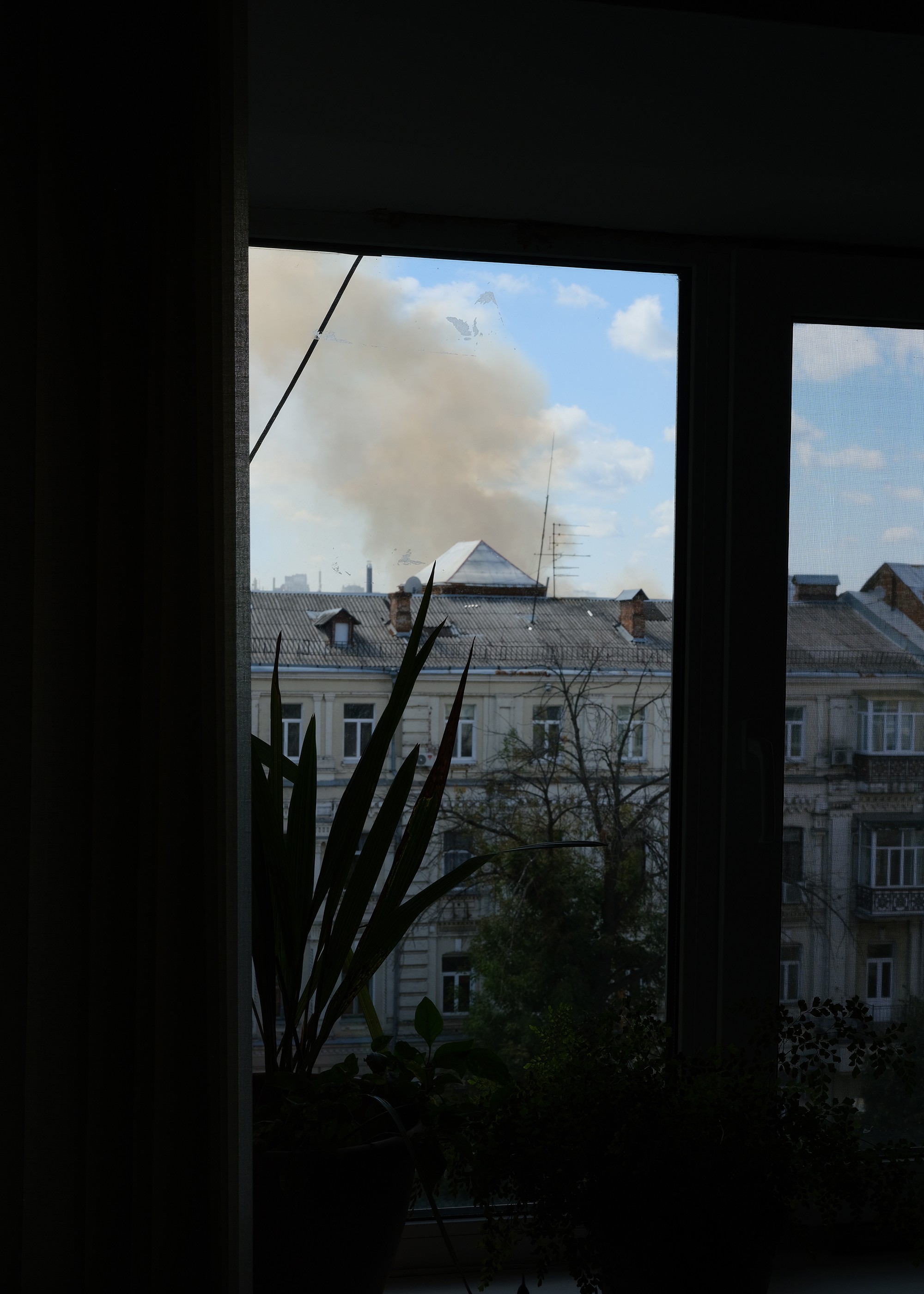 photo of view out the window over neighboring roofs with smoke rising nearby