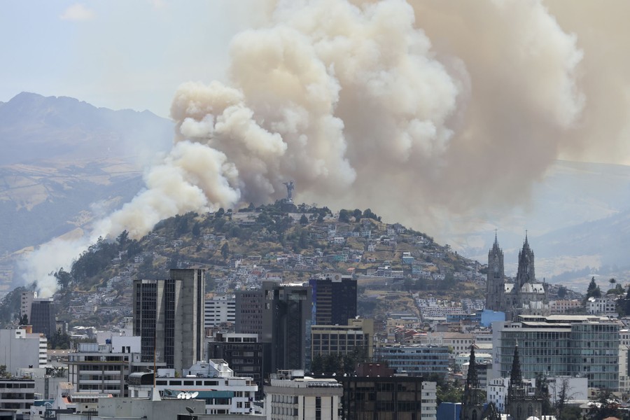Smoke billows above a small hill covered in many houses.