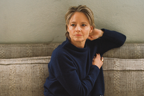 A portrait photograph of the actor Jodie Foster curled up barefoot on a couch, wearing jeans and a navy-blue sweater.