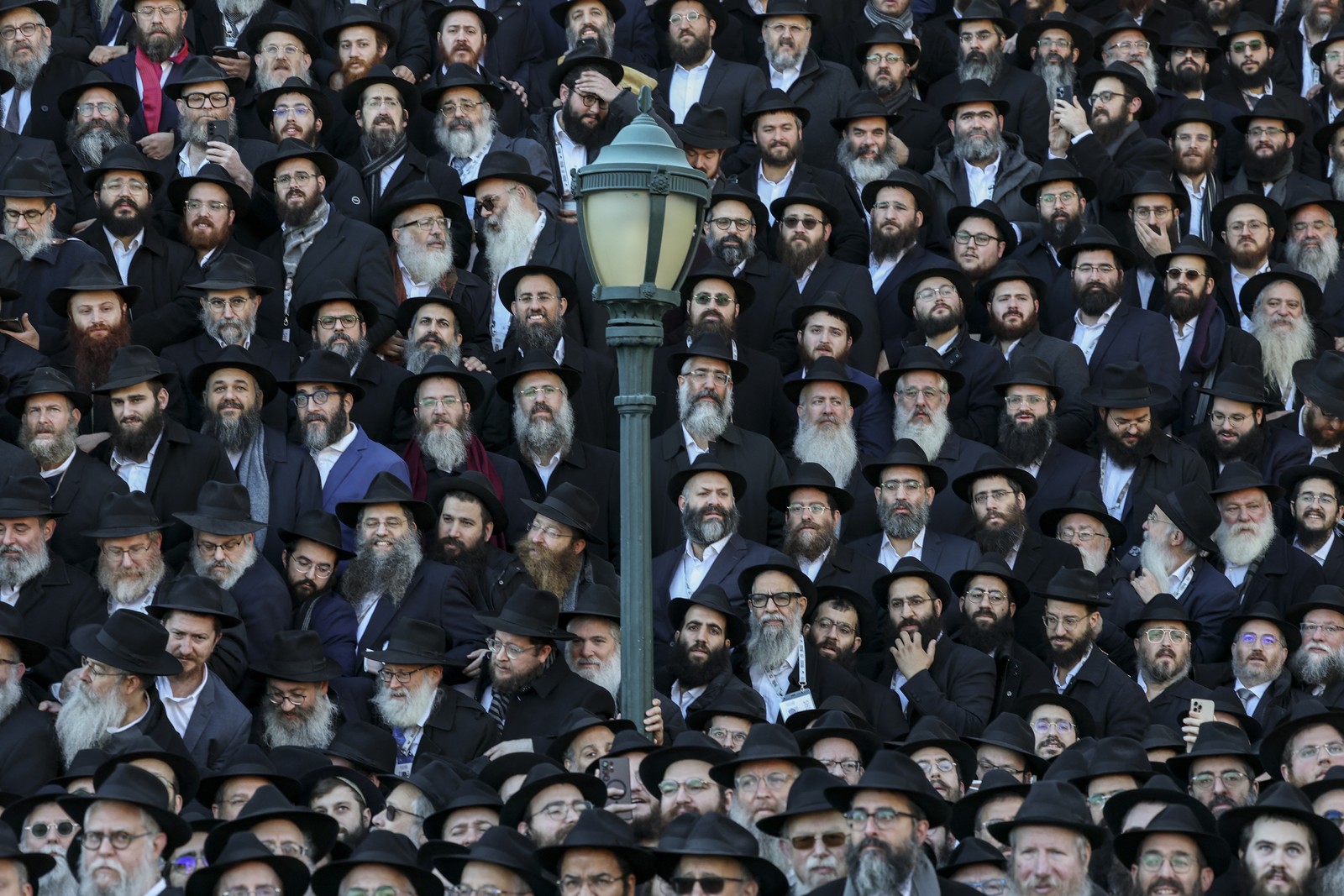 Dozens of rabbis wearing black coats and black hats stand side-by-side, and in tall rows, for a group portrait.