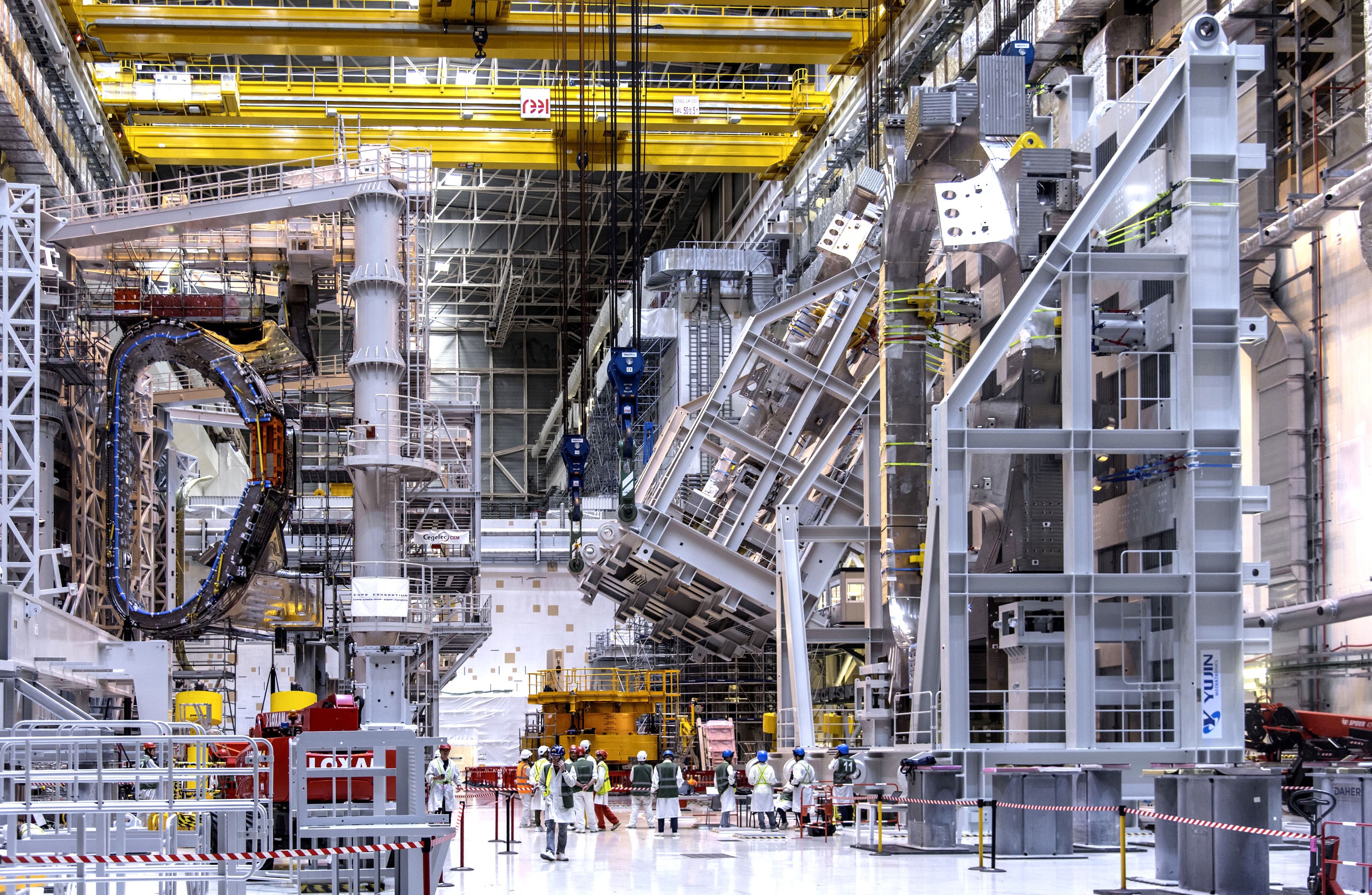 People stand inside a large open building beside huge rigs and machinery being assembled