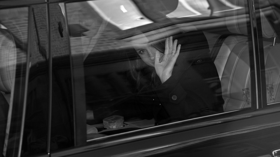 A black-and-white photo of Meghan Markle waving from inside a car.