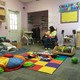A woman holds a baby in a room filled with colorful toys and rugs.