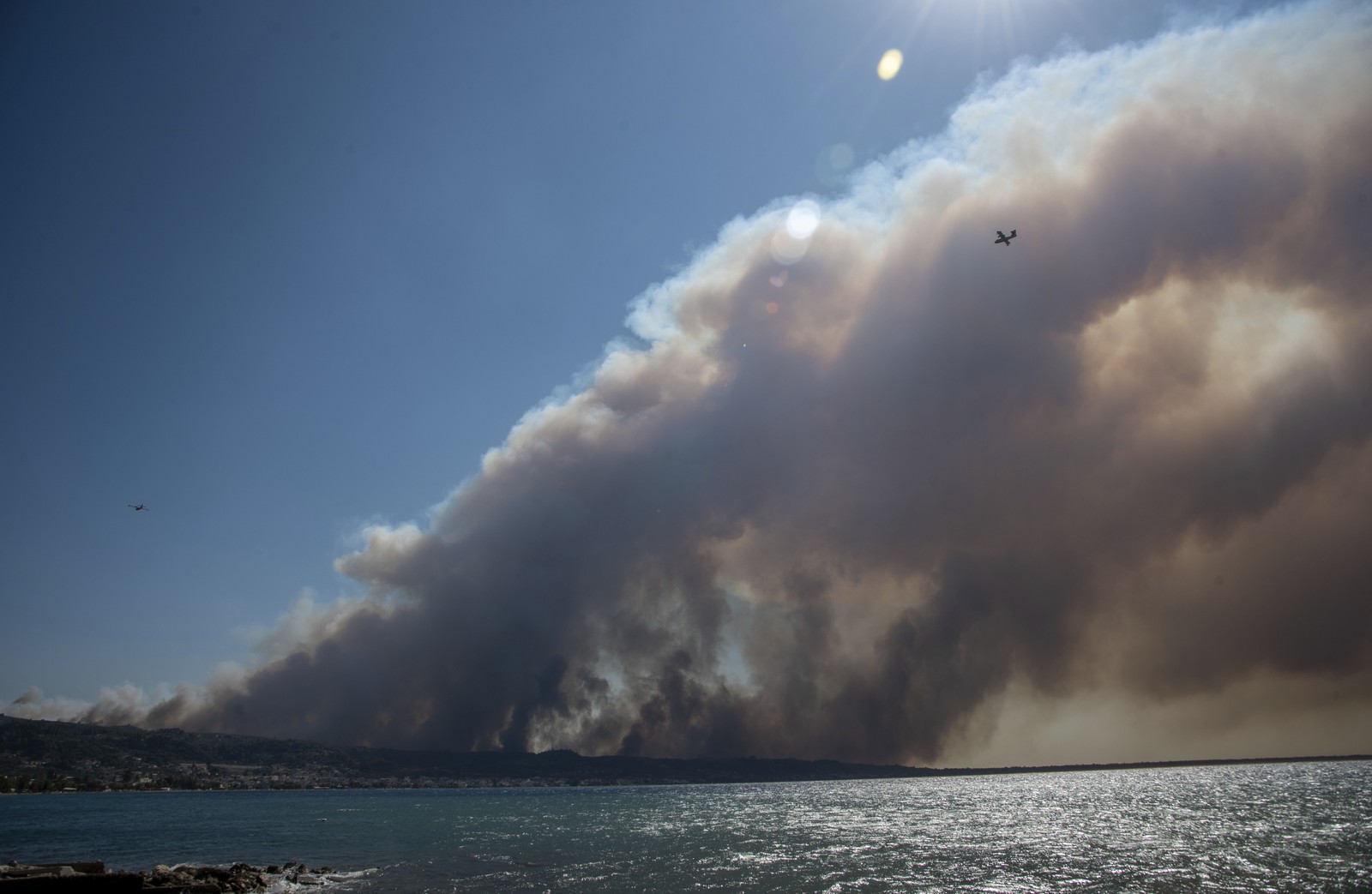 Smoke from a wildfire covers the sky above a seaside village.