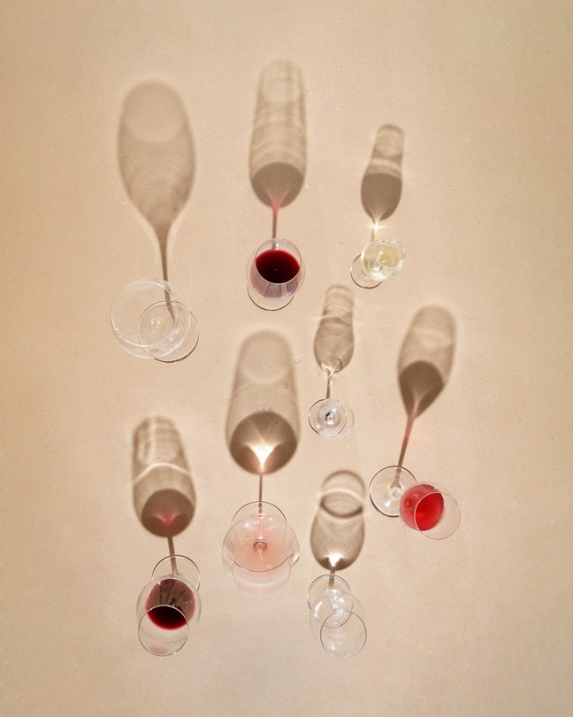 Photograph of eight partially full wine glasses casting shadows on a beige background