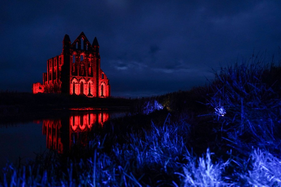 The ruins of an abbey stand in a field at night, illuminated from below with red light, looking very spooky.