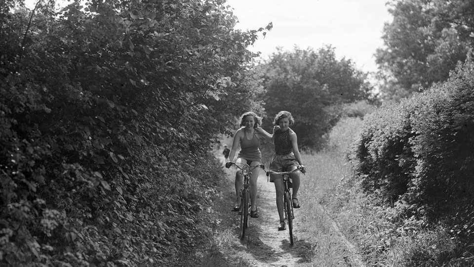Black-and-white photograph of two people riding bikes down a wooded path