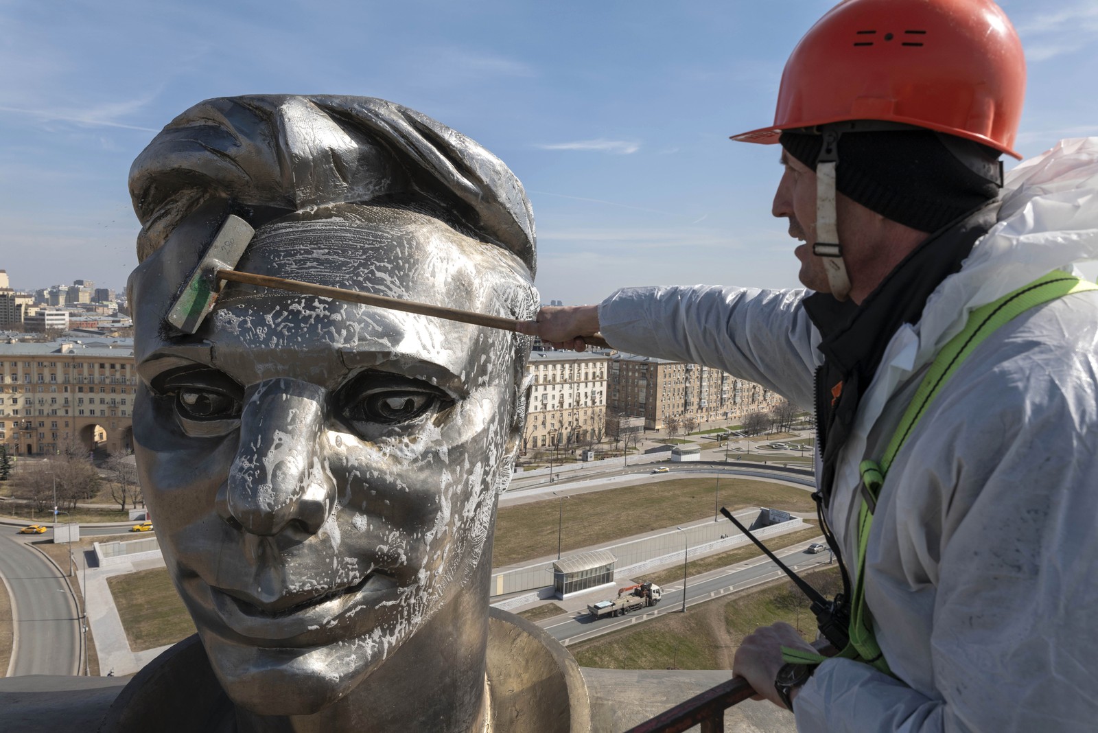 A cleaner uses a brush on the soap-covered face of a large statue.