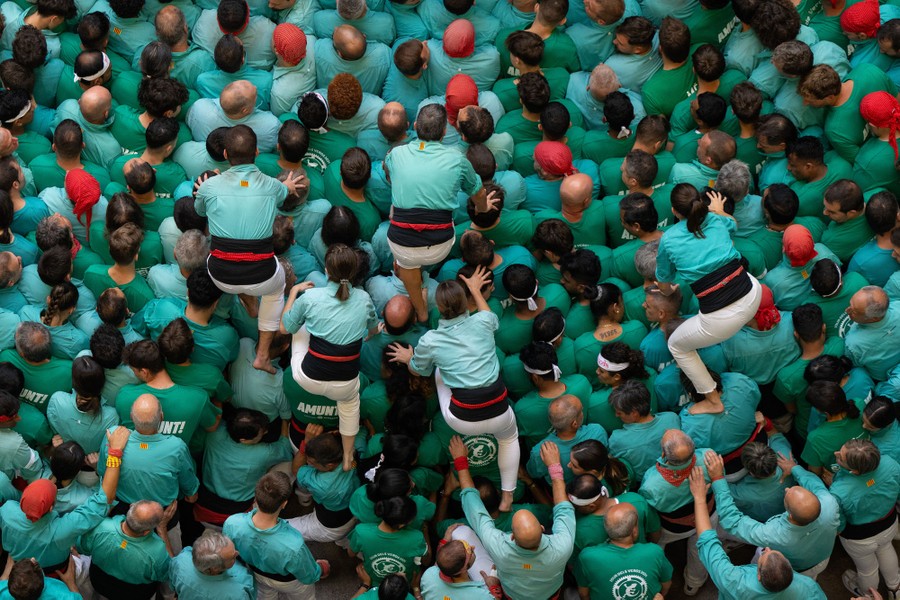 Four people climb across the shoulders and heads of a crowd of green-shirted people.