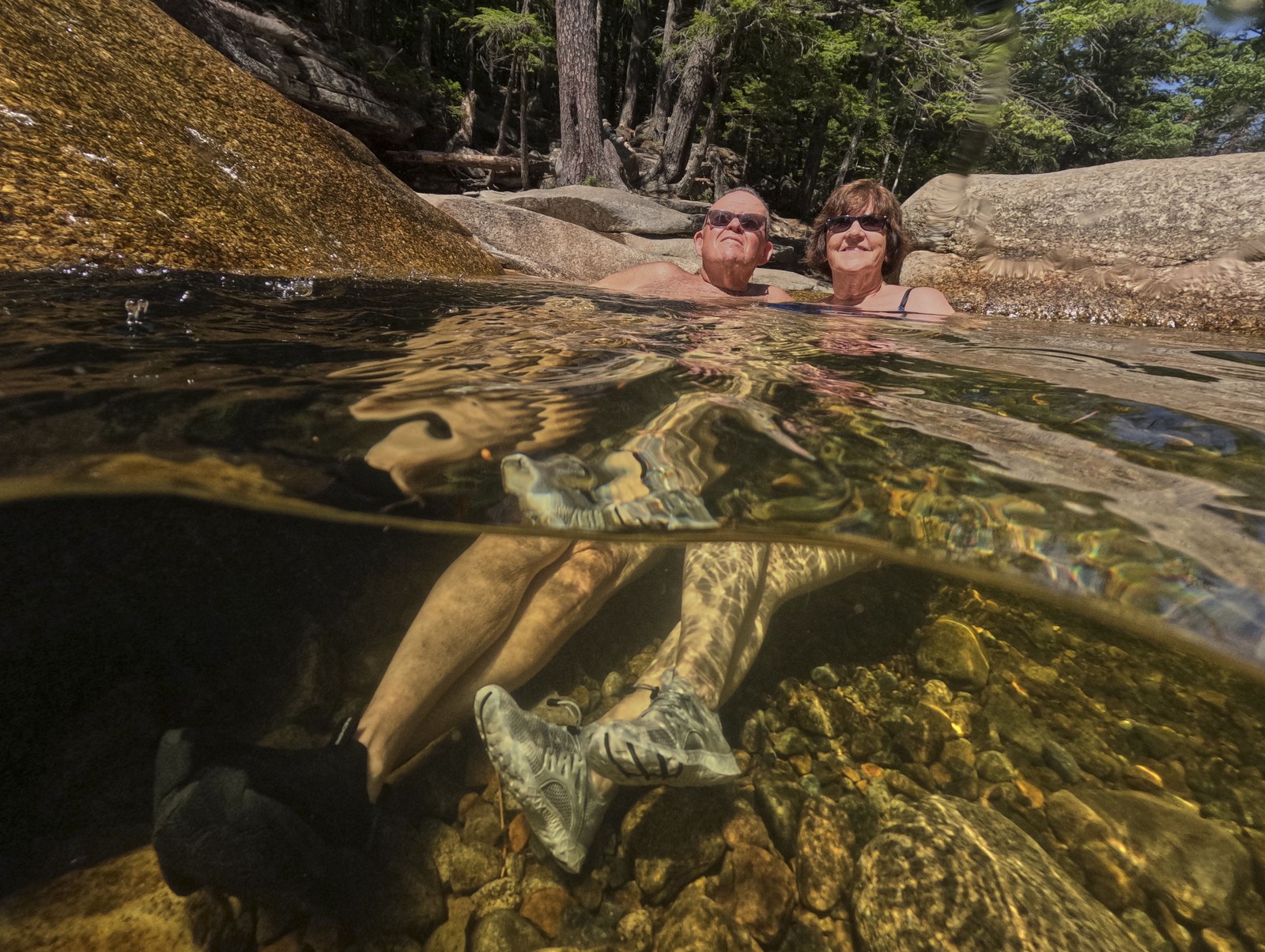 Two people sit side-by-side in a pool of water, seen both above and below the water.