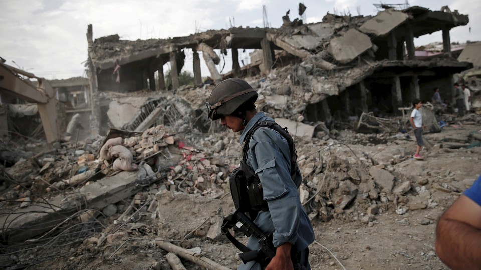 An Afghan policeman walks past a ruined building and a pile of rubble.