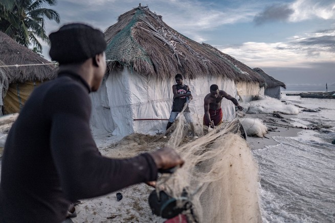Fishermen prepare their nets while a rising tide approaches nearby homes on the island of Nyangai. 