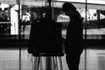 A photo of a voter in silhouette using a voting booth at a polling station