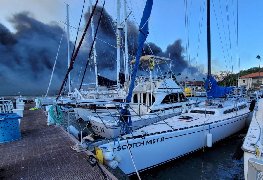 Smoke rises, seen behind boats in a marina.