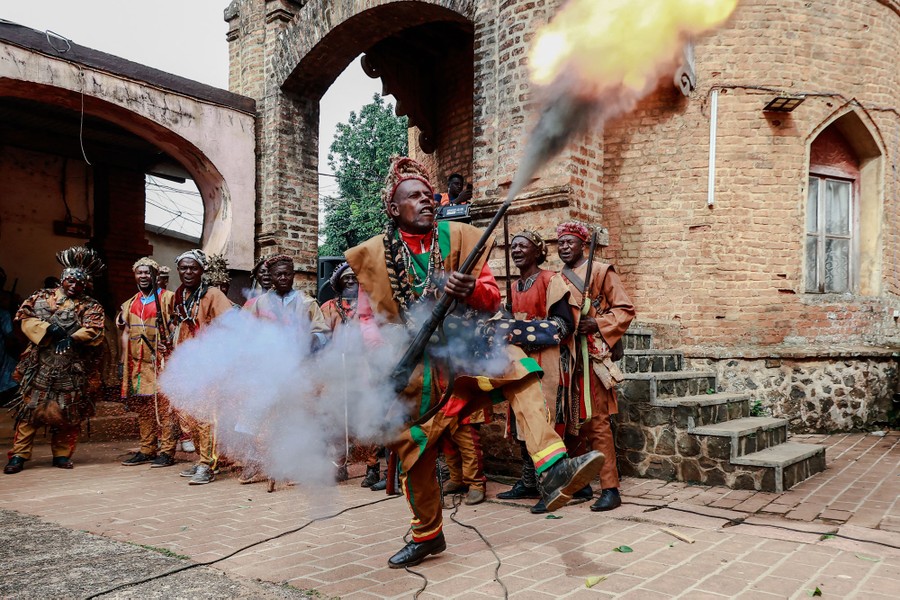 A person in traditional clothing fires a weapon into the air in a courtyard.